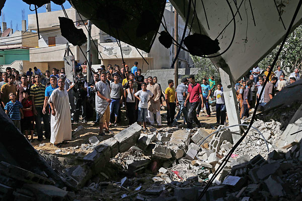 Палестинцы собираются вокруг дома, который был разрушен в результате бомбардировок израильских ВВС на юге сектора Газа.