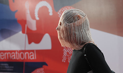 Режиссер Ольга Дарфи достала из сумки мешок с прорезями для глаз и надела его перед тем, как ступить на дорожку. К ней бросились журналисты, но охранники их оттеснили. Женщина беспрепятственно прошла в зал, где началась церемония открытия