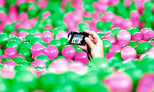 Посетитель снимает на камеру бассейн, заполненный зелеными и розовыми шариками.