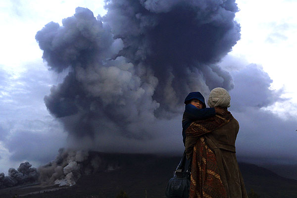 Деревня Берастепу. Женщина с ребенком на руках наблюдает за выбросом пепла вулкана Синабунг на севере Суматры.