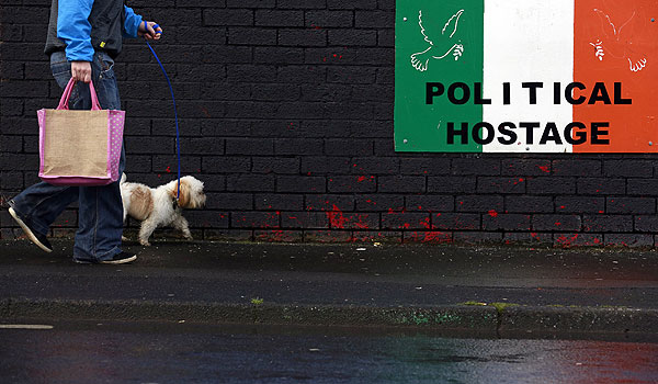 Женщина идет с собакой мимо стены с граффити в одном из городков Северной Ирландии.