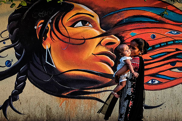 Женщина с ребенком стоит у стены с граффити в Мумбаи.