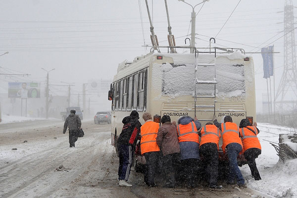 Работники коммунальных служб толкают троллейбус во время сильного снегопада в Челябинске.