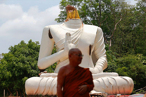 Буддийский монах стоит перед разрушенной статуи Будды на севере Таиланда.