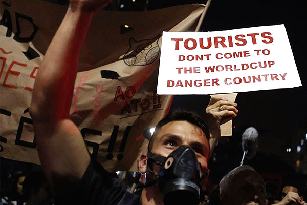 Демонстрант в респираторе, за ним плакат со словами: "Туристы, не приезжайте на Чемпионат мира. В стране опасно".