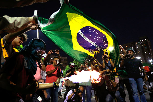 Демонстранты поджигают флаг Бразилии.