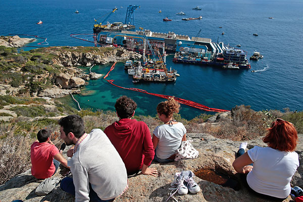 Туристы смотрят сверху на затонувший лайнер.