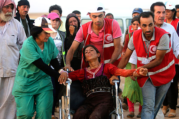 Сотрудники курдского отделения Красного Полумесяца помогают женщине на инвалидном кресле.