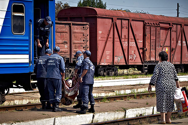 Сотрудники МЧС Украины помогают поднять пожилую женщину в вагон.
