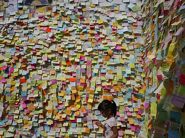 Девочка стоит у стены, оклеенной стикерами с посланиями от протестующих в Гонконге.