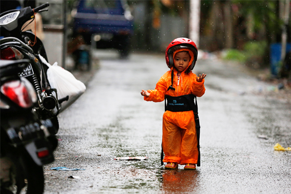 Мальчик в шлеме и плаще ловит капли дождя в городе Банда-Ачех, Индонезия