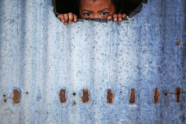 Ребенок выглядывает из самодельного железного укрытия, заменяющего дом. Разрушительный тайфун Хайян в 2013 году практически полностью уничтожил филиппинский город Таклобан, оставив без крова около двух миллионов его жителей.