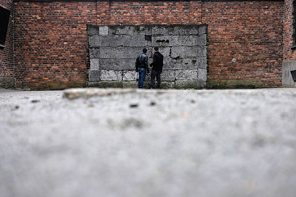 Посетители Государственного музея Аушвиц-Биркенау у воссозданной "стены смерти", где расстреливали узников после допросов