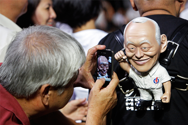 Сторонник партии "Народное действие" фотографирует фигуру Ли Куан Ю во время предвыборного митинга в Сингапуре, май 2011 год