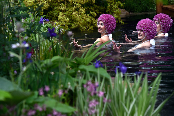 Выступление синхронисток в пруду, окруженном цветами, во время предпоказа шоу