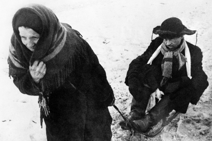 Пожилая женщина везет на санках истощенного от голода мужчину во время блокады города. 1942 год.