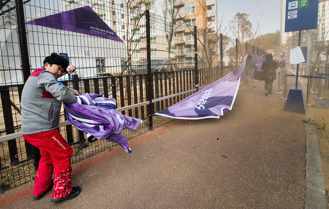 Олимпийский работник укрывается от сильных порывов ветра в олимпийской деревне в Канныне