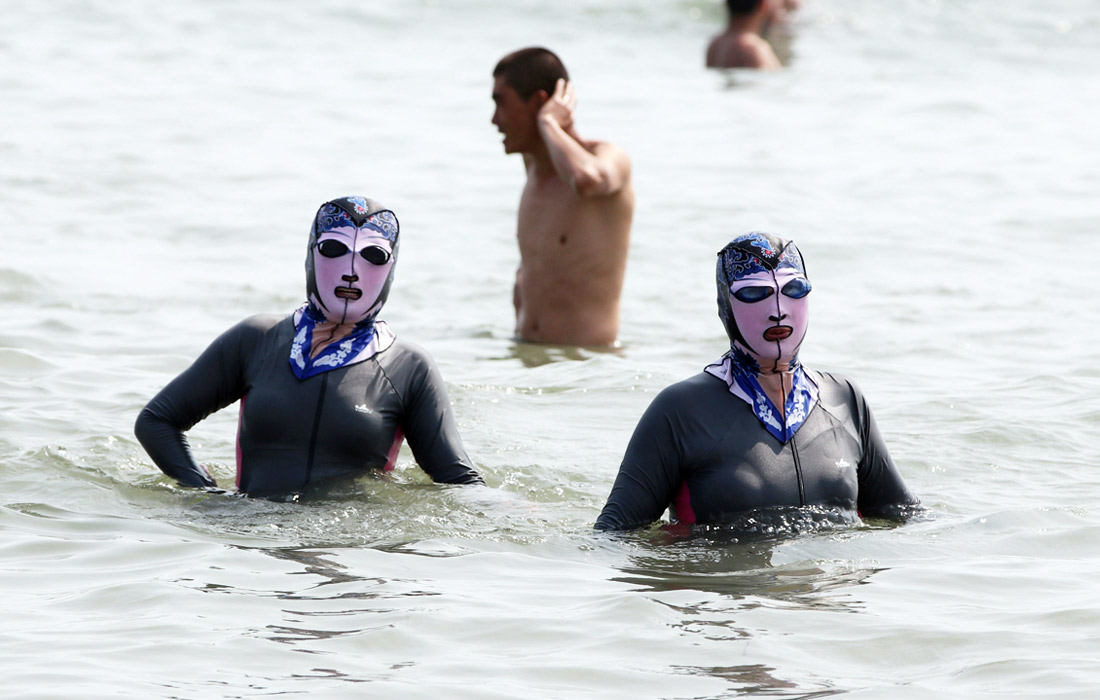 Пляжный отдых на побережье Желтого моря в китайском Циндао. Отдыхающие надевают резиновые маски с прорезями для глаз, рта и носа, защищающие кожу от солнечных лучей.