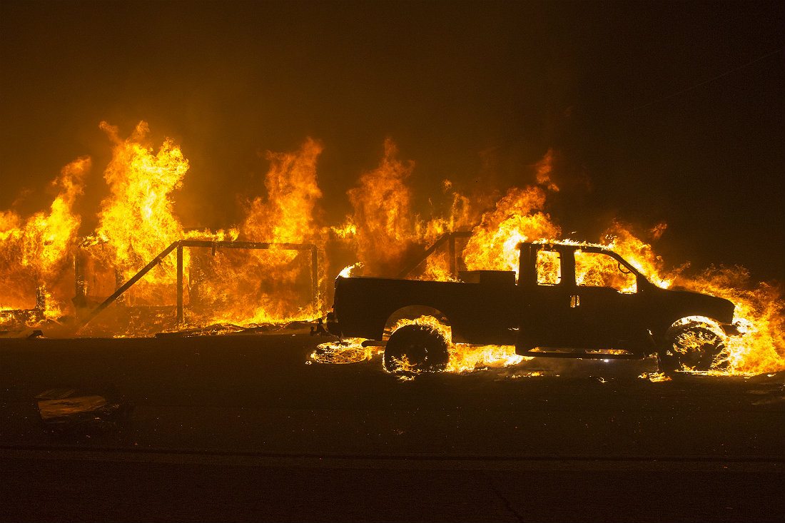 Горящая машина на улицах уничтоженного пожаром города Парадайс в Калифорнии