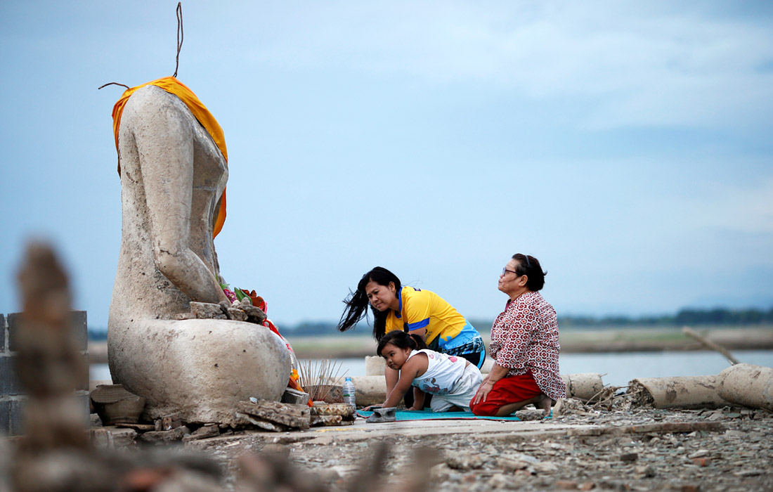 Паломники молятся у разрушенной статуи Будды, появившейся на месте обмелевшего водохранилища в провинции Лопбури, Таиланд