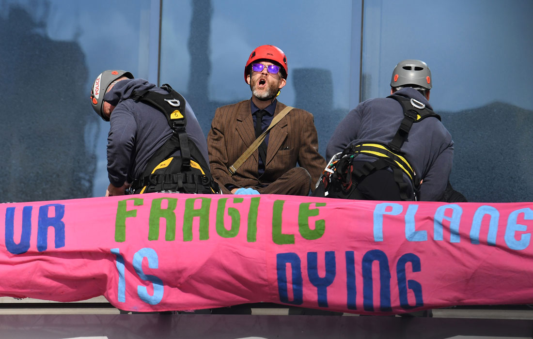 Протестующий Extinction Rebellion стоит на крыше аэропорта, пытаясь заблокировать Лондонский хаб