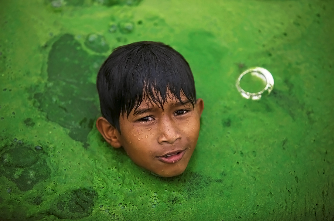 Непальский мальчик купается в озере, покрытом водорослями
