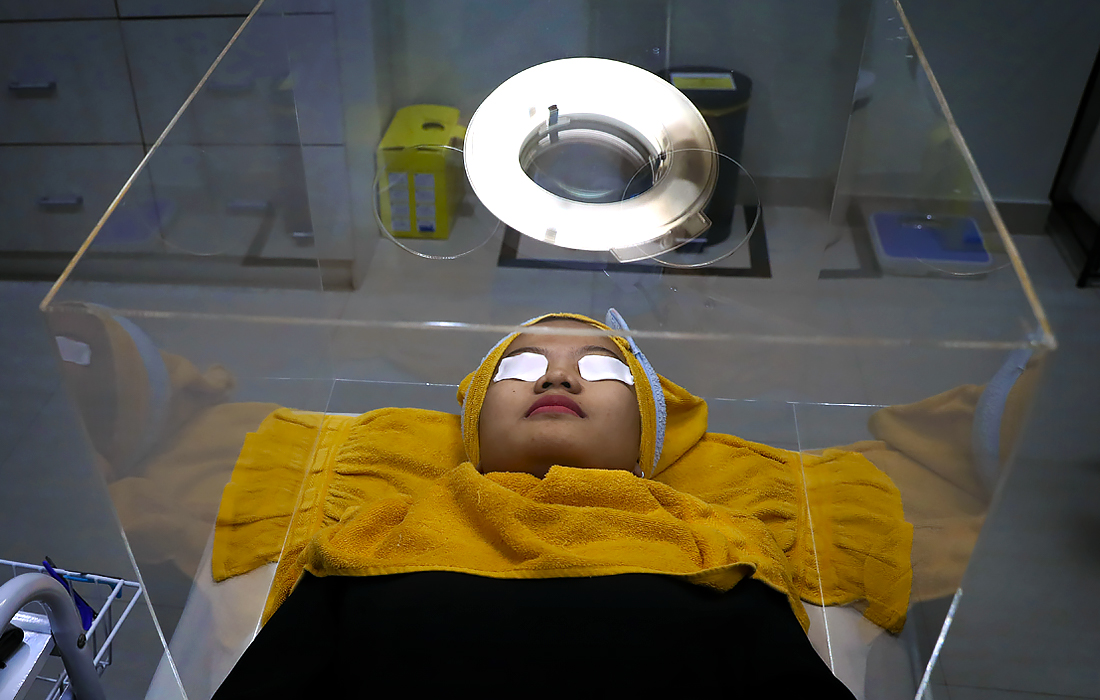 25 июня. Пациентка ожидает приема в клинике красоты в Джакарте в защитном боксе, используемом в качестве меры предосторожности.