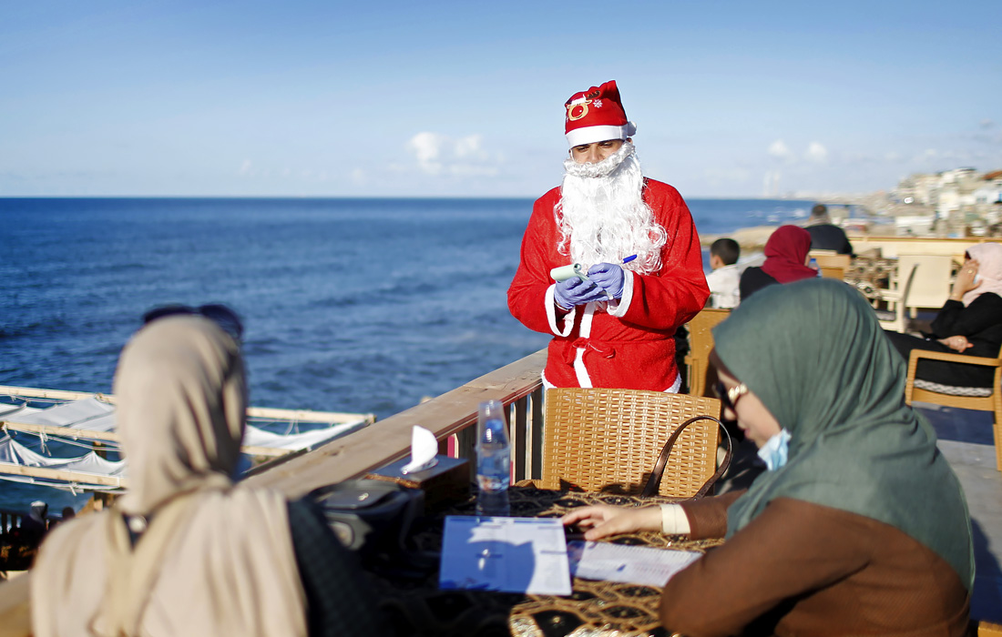 Официант в костюме Санта-Клауса принимает заказ в кафе на пляже в городе Газа