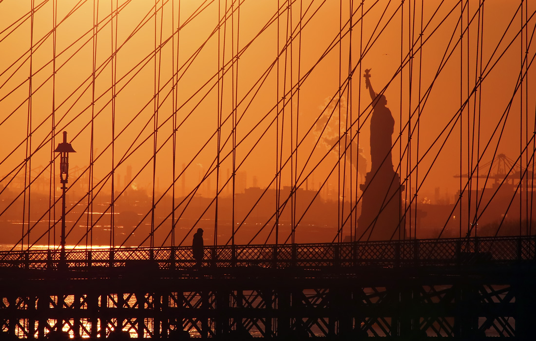 Солнце садится за Бруклинским мостом в Нью-Йорке