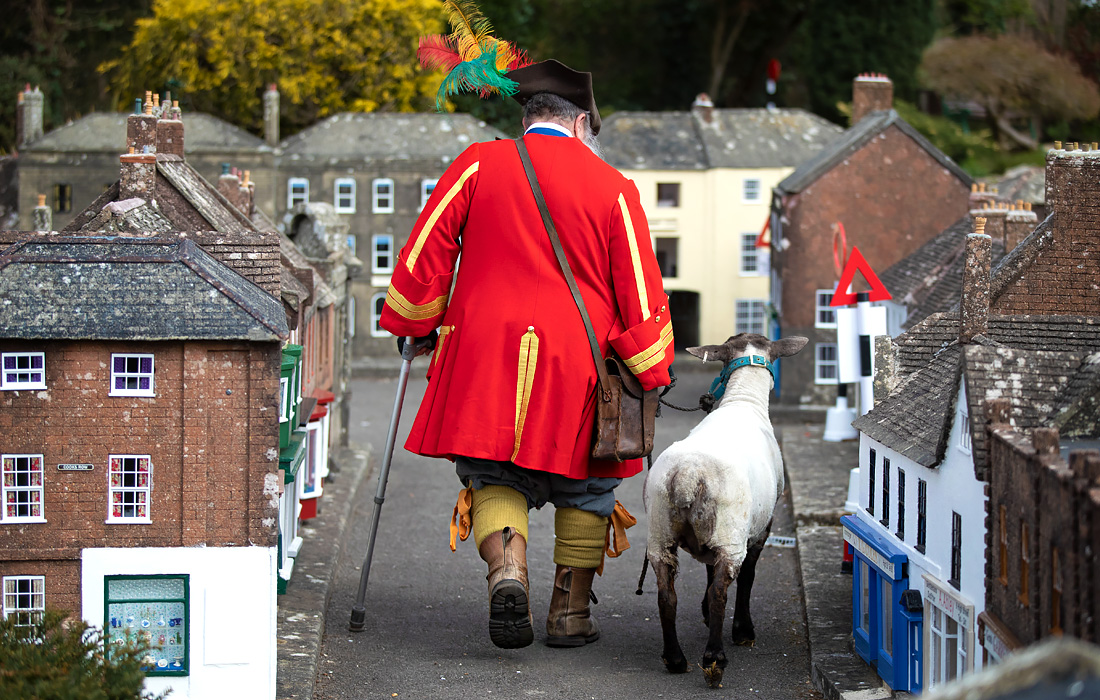 Глашатай Уимборн-Минстера на юго-западе Англии ведет овцу через игрушечный город, который снова откроется для посетителей с 12 апреля