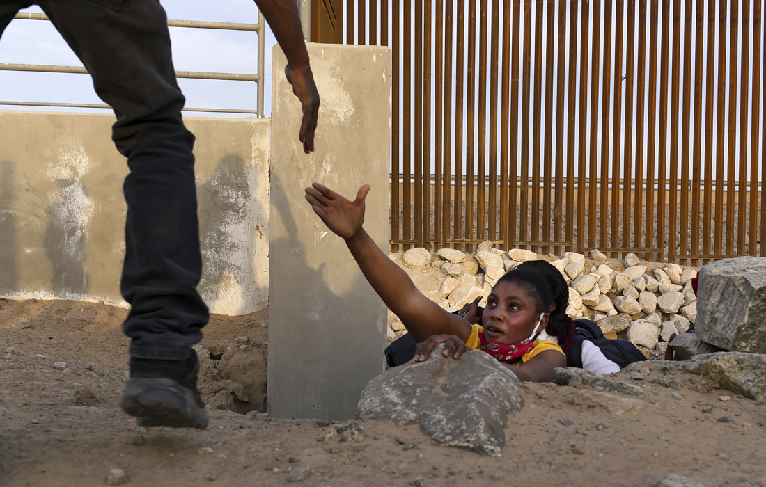 Мигрантка из Гаити пролезает под пограничной стеной США в Юме, штат Аризона