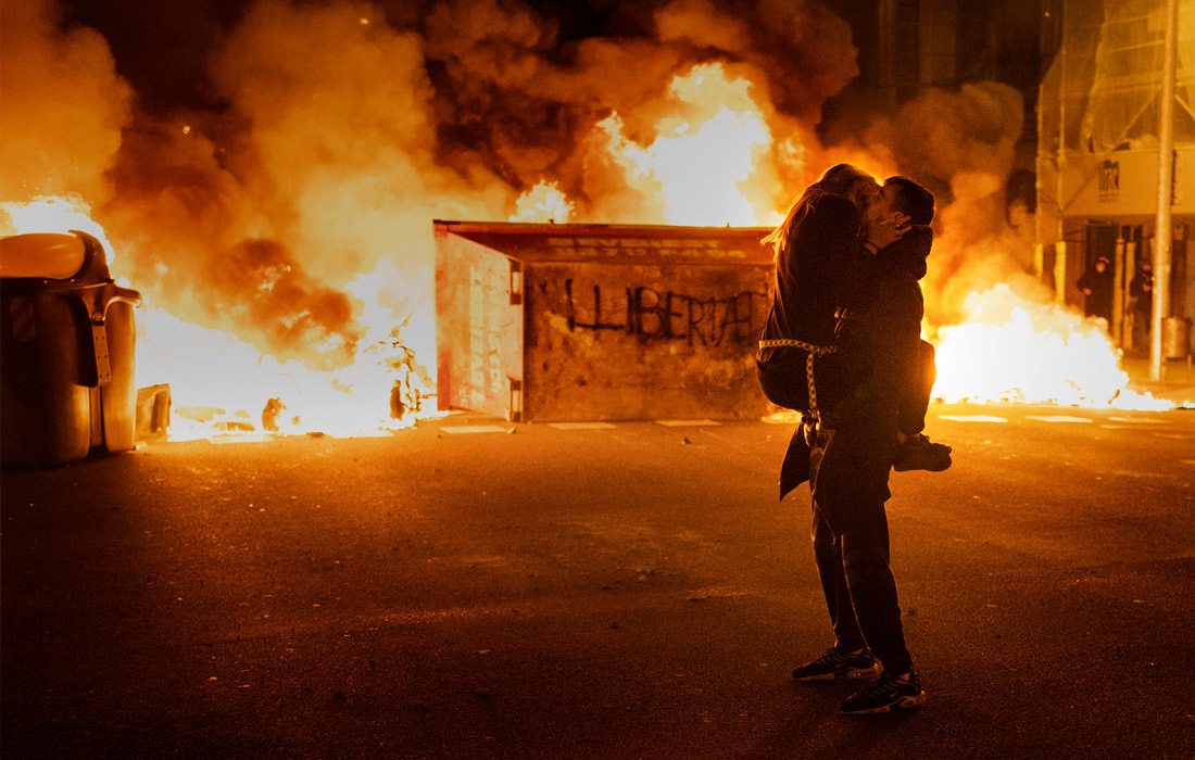 Пара демонстрантов перед горящей баррикадой во время протестов против ареста рэп-музыканта Пабло Хаселя в Барселоне