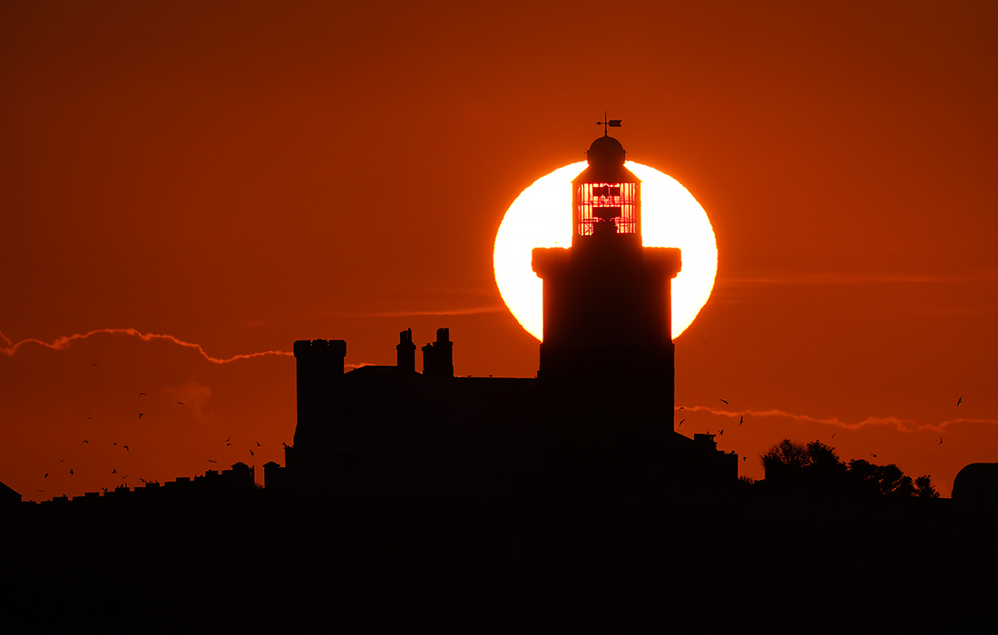 Солнце встает над маяком на острове Коке, Великобритания