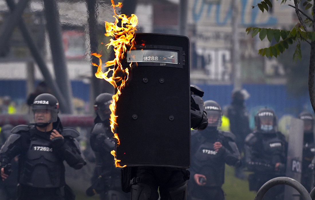 В Боготе офицер полиции держит щит, который загорелся из-за брошенного протестующим коктейля Молотова