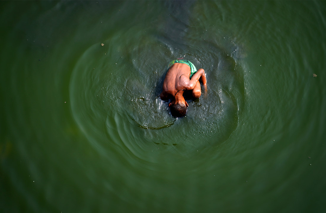 Мальчик ищет монеты, брошенные в качестве религиозных подношений в реку Ямуна, в жаркий день в Нью-Дели