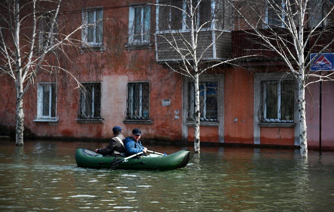 Мужчины передвигаются на надувной лодке на одной из подтопленных улиц в Орске