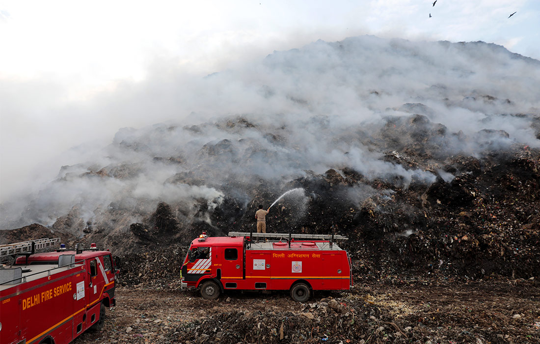 Индийские пожарные пытаются потушить пламя на мусорной свалке в Газипуре
