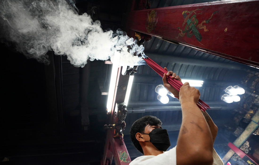 Мужчина зажигает ароматические палочки в Бангкоке, Таиланд