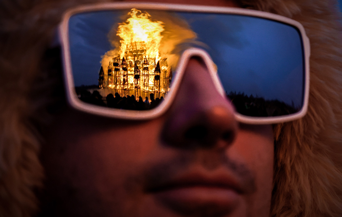 Участник масленичных гуляний наблюдает за сожжением арт-объекта в парке "Никола-Ленивец"